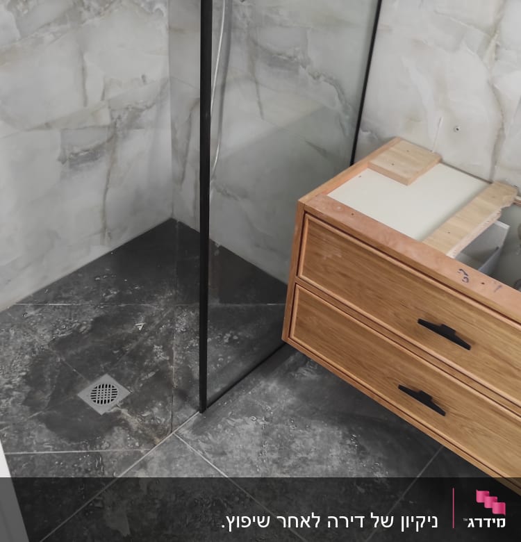 מקלחון זכוכית עם רצפה מלוכלכת וארון עץ